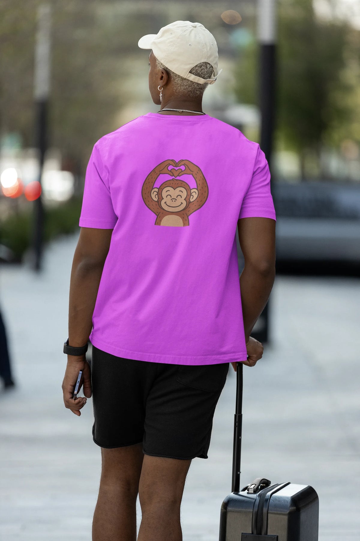 Lavender oversized T-shirt with cartoon monkey heart-hands graphic print, back view on male model walking with suitcase